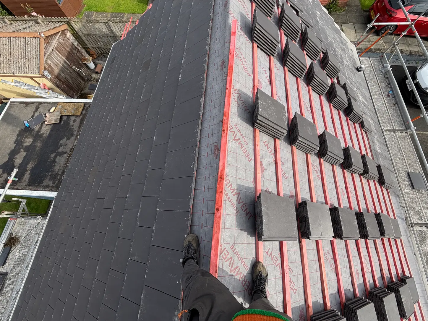 Dark slate tiles being laid over Permavent breathable membrane and red battens, viewed from the roof slope