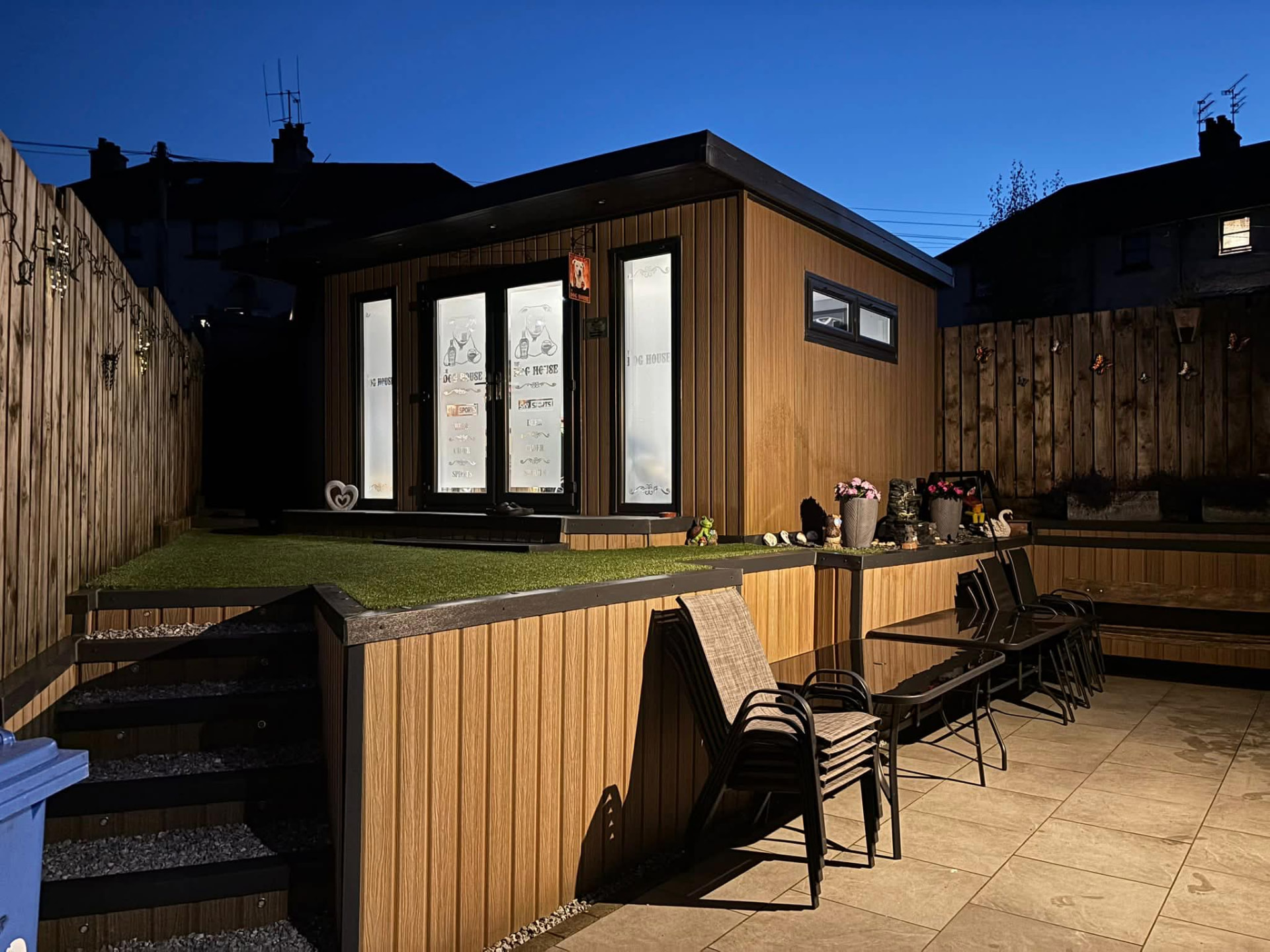 Timber-clad garden room with glazed double doors, decking and raised lawn, built as a home bar and entertaining space