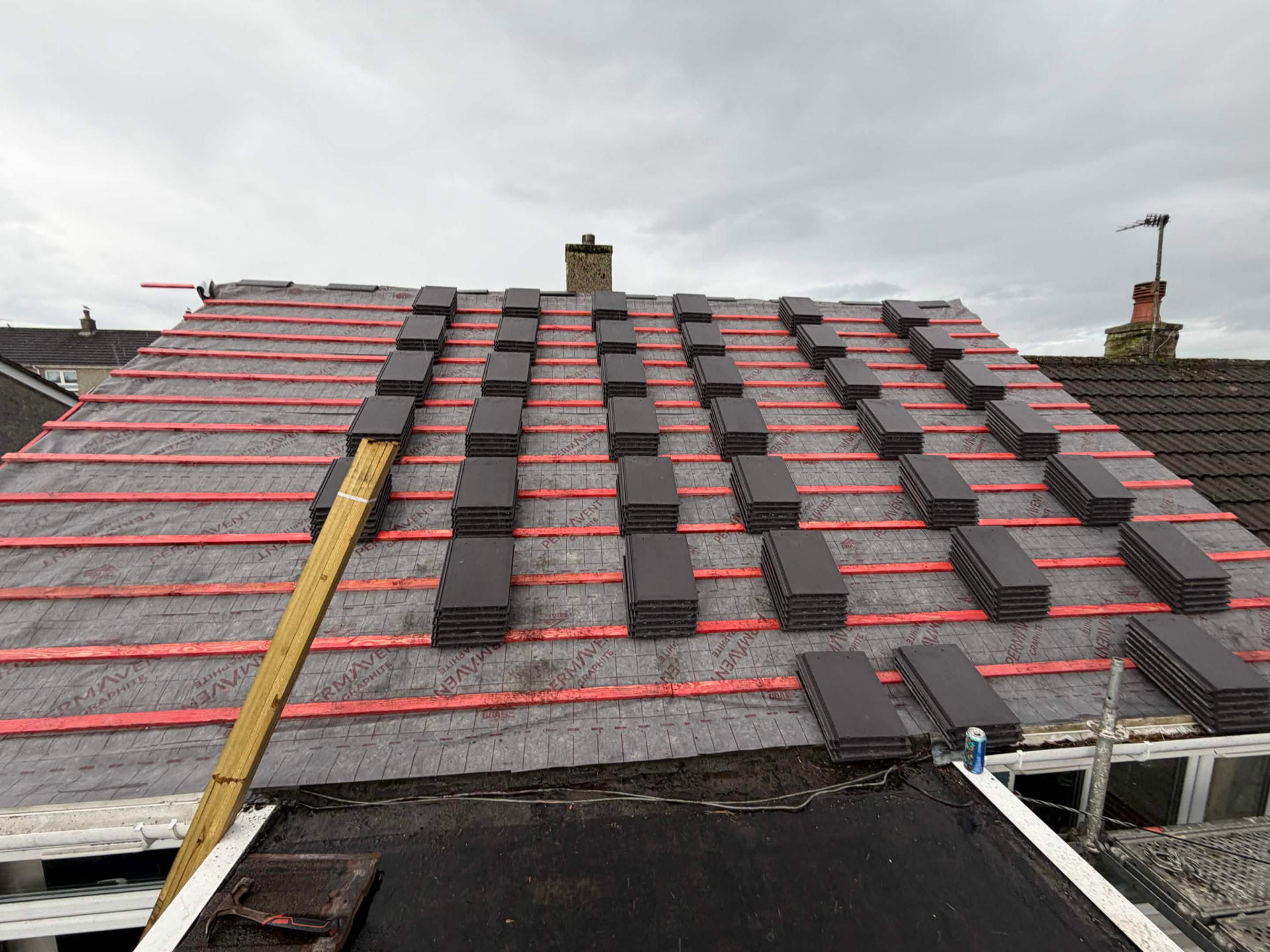 Roof tiling in progress with stacks of dark tiles and breathable membrane
