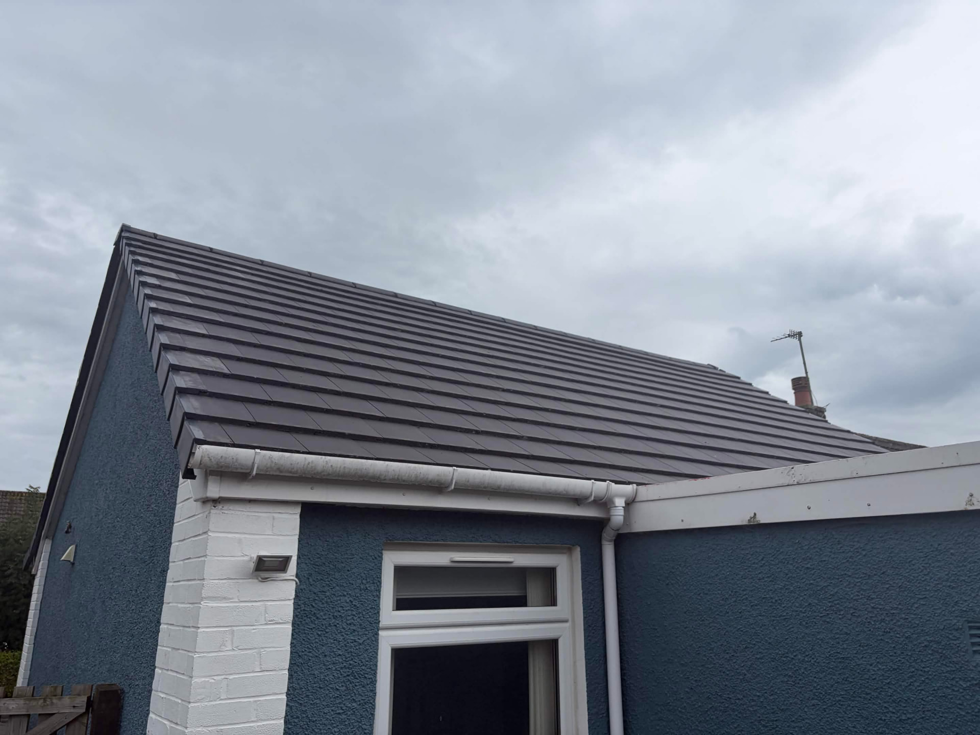 New dark grey roof tiles and white guttering on a rendered house under a cloudy sky